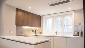 A modern kitchen with white cabinetry, a built-in oven, a sink, and a window with blinds. - Stunning Rare Soho Gem (London)