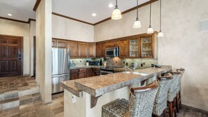 A kitchen with granite countertops, stainless steel appliances, wooden cabinets, and a bar area with wicker stools. - Excellent location in Mountain Village core, spacious and cozy condo (Mountain Village)