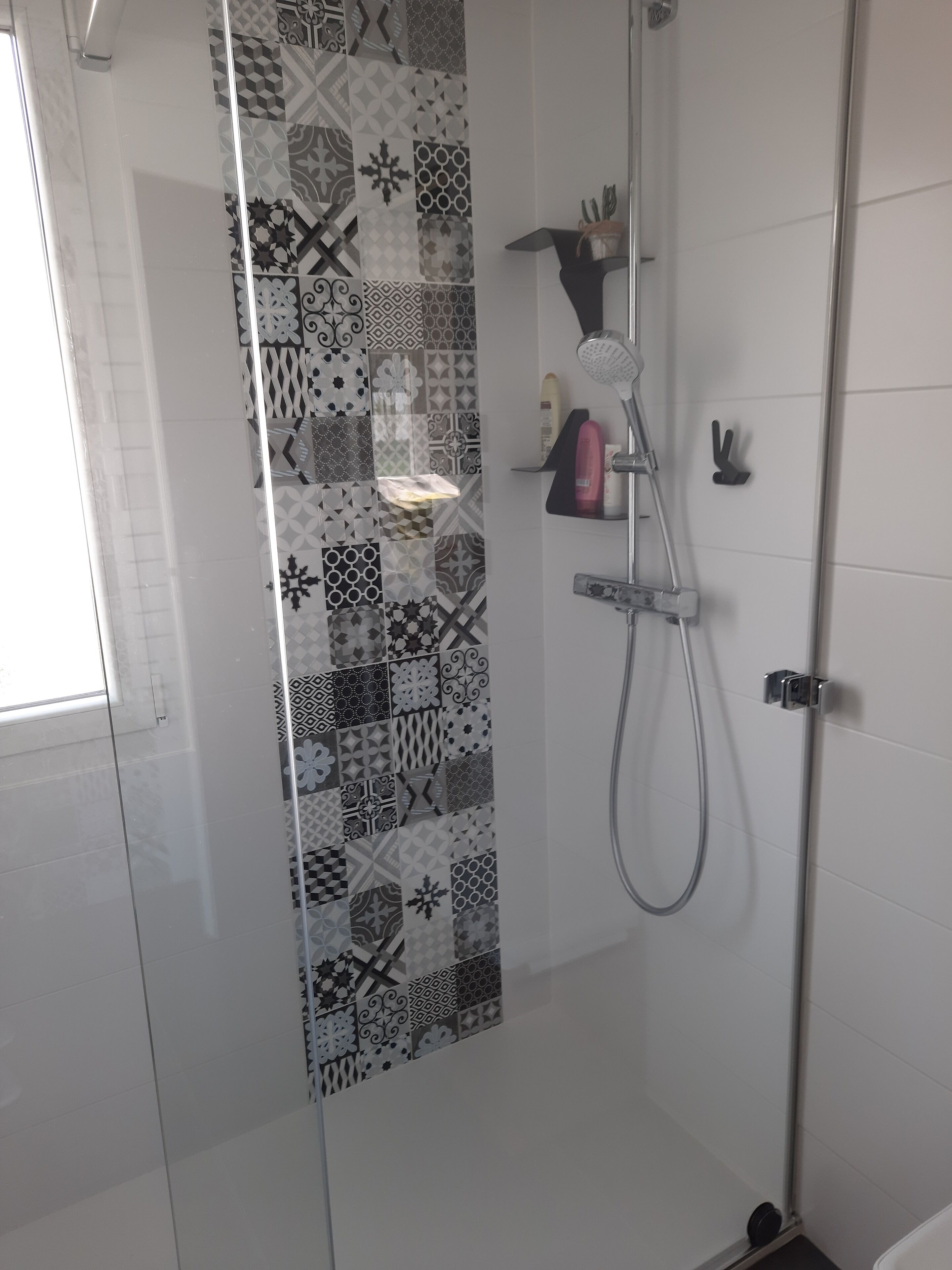A shower with a glass door, a showerhead, and a hand soap dispenser on a shelf.