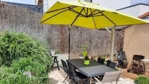 An outdoor patio with a table and chairs, a yellow umbrella, and potted plants.