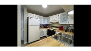 A compact kitchen with white cabinets, a stainless steel sink, a refrigerator, a microwave, and a stove. - Mountain View 2BR Condo - No Cleaning Fee - Close to Downtown (Gatlinburg)