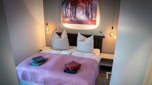 A neatly made bed with a pink quilt, two white pillows, and folded towels. - Modern vacation home with terrace and outdoor sauna (Schermbeck)