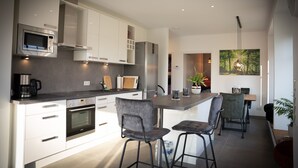 A modern kitchen with white cabinets, a built-in oven, and a central island with bar stools. - Modern vacation home with terrace and outdoor sauna (Schermbeck)