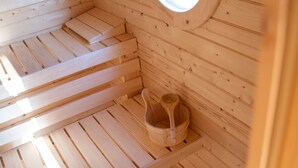 A wooden sauna with a circular skylight, wooden benches, and a wooden bucket. - Modern vacation home with terrace and outdoor sauna (Schermbeck)