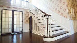 A grand staircase with white balusters and dark wood steps, leading to a landing with a patterned wallpaper wall and a large window.