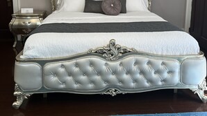 A large, ornate bed with a tufted headboard, a matching footboard, and a decorative canopy.