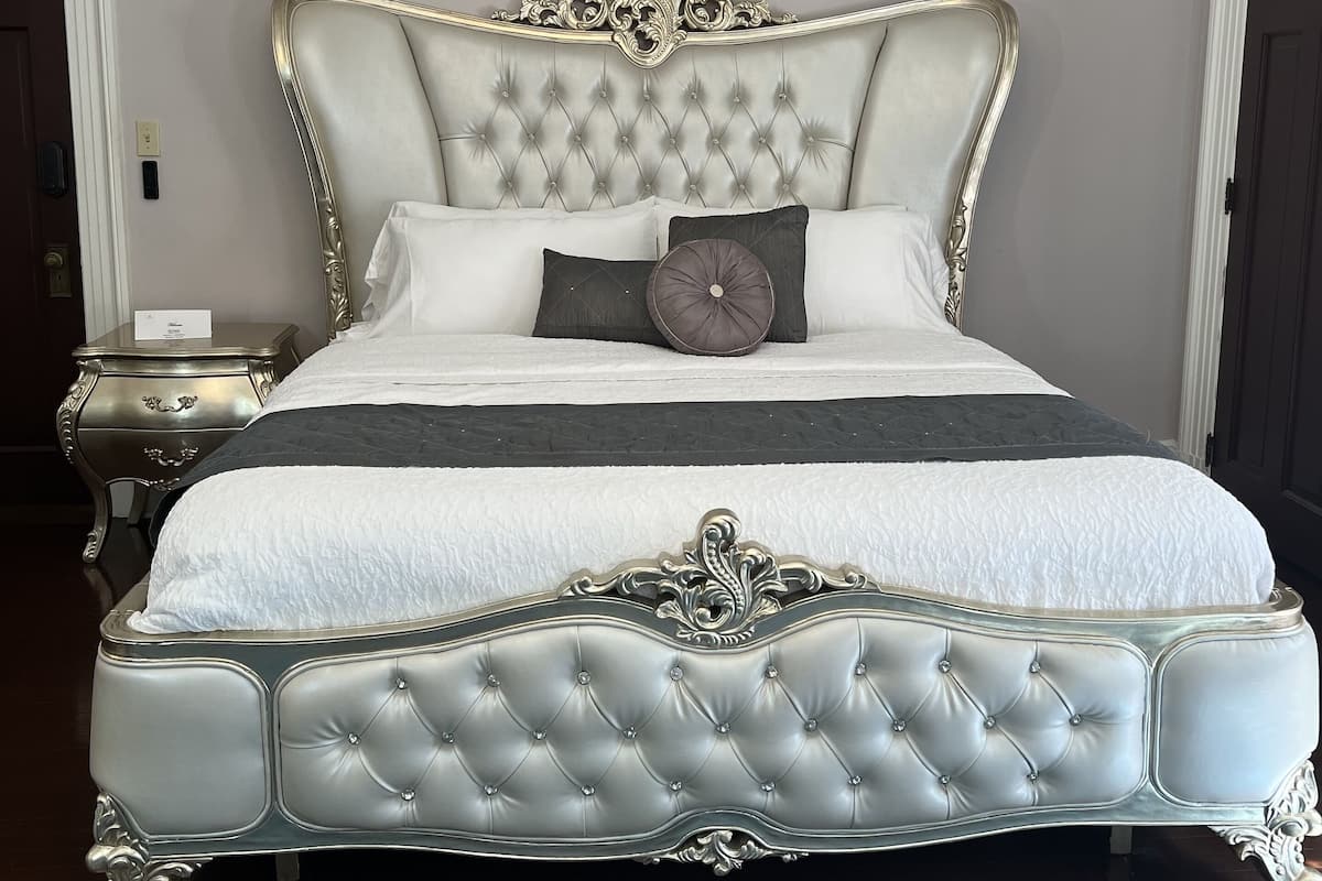 A large, ornate bed with a tufted headboard, a matching footboard, and a decorative canopy.