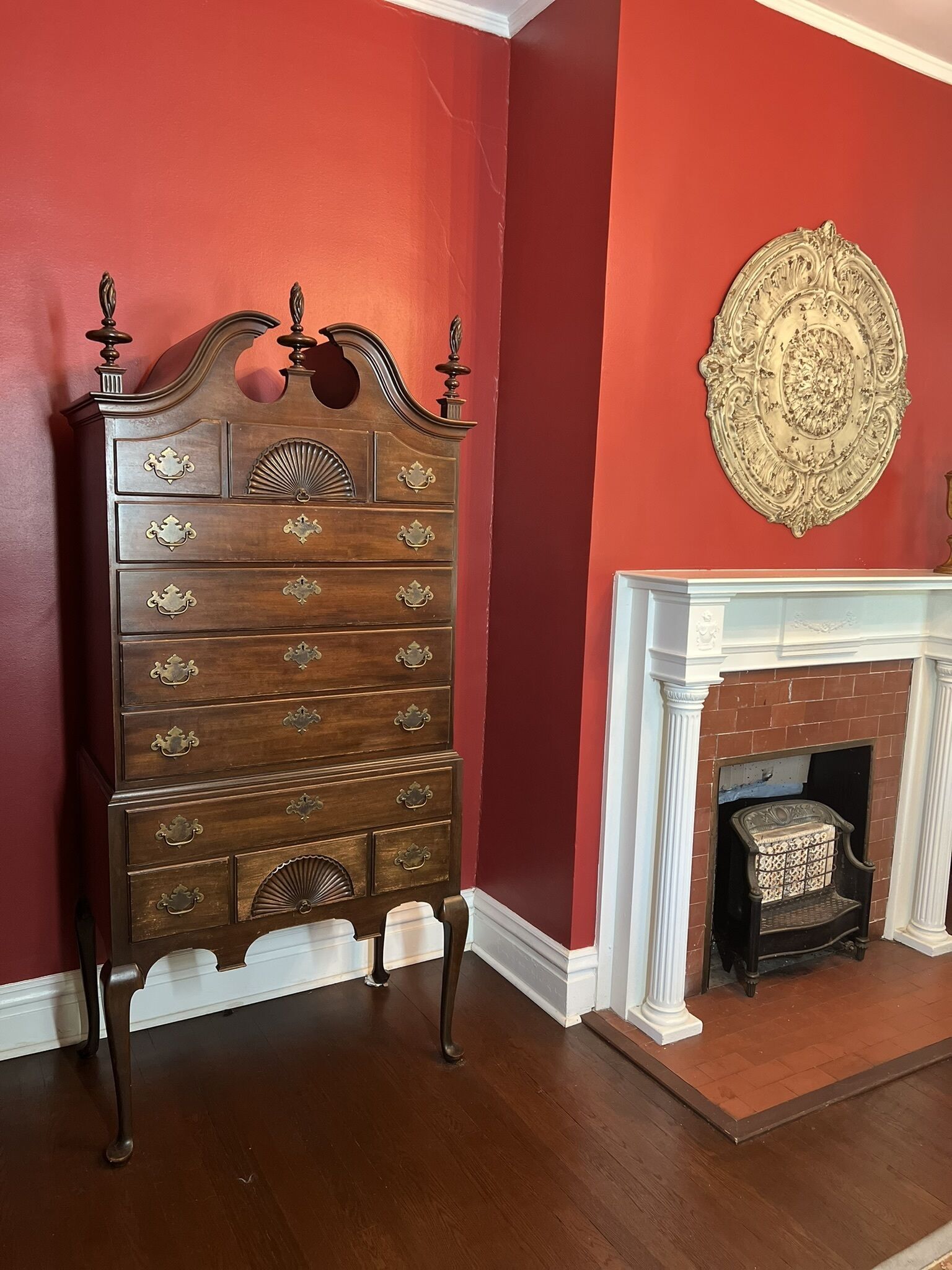 A wooden dresser with ornate handles and a decorative top, positioned next to a fireplace with a white mantel and a patterned rug.