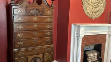 A wooden dresser with ornate handles and a decorative top, positioned next to a fireplace with a white mantel and a patterned rug.