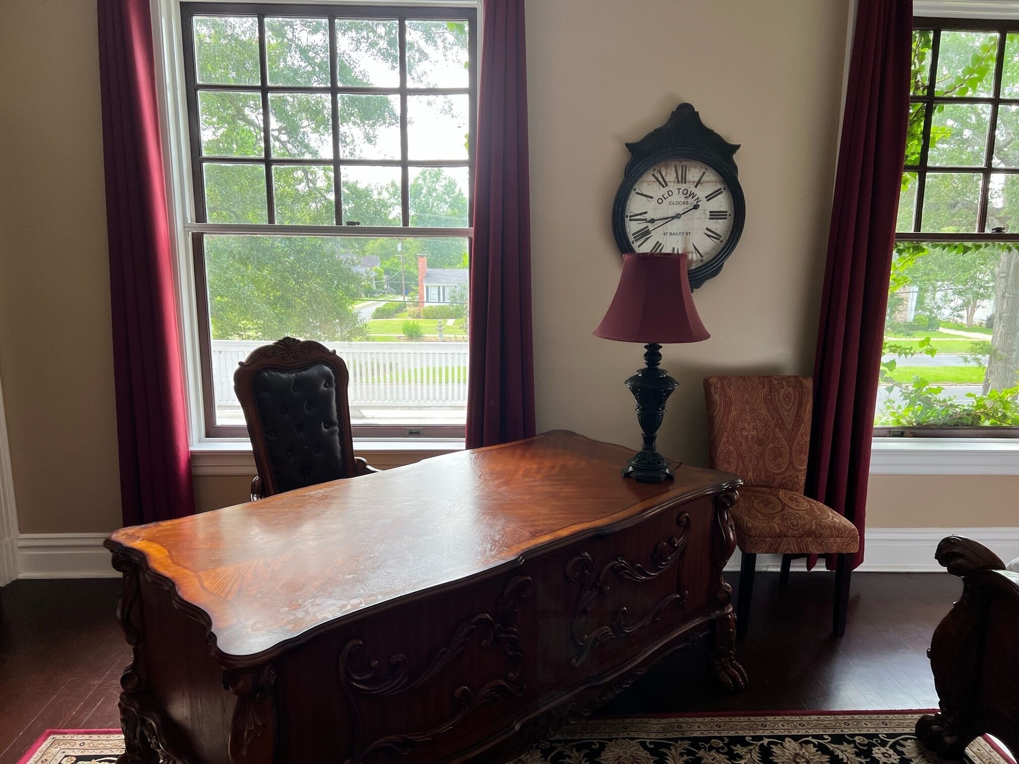 A room with a wooden desk, a chair, a clock, and a window with curtains.