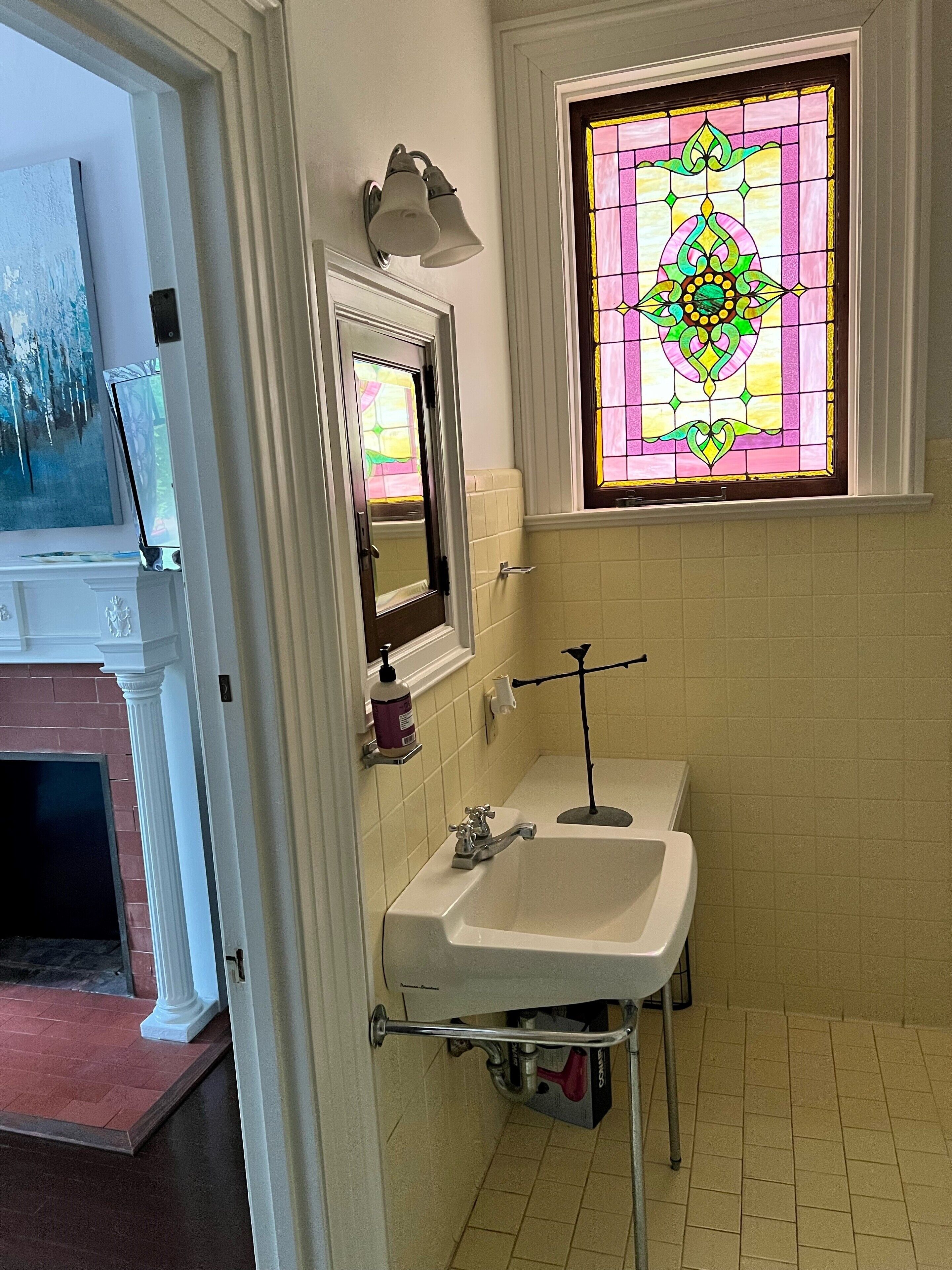 Un baño con un lavamanos blanco, un espejo y una ventana con vitral.