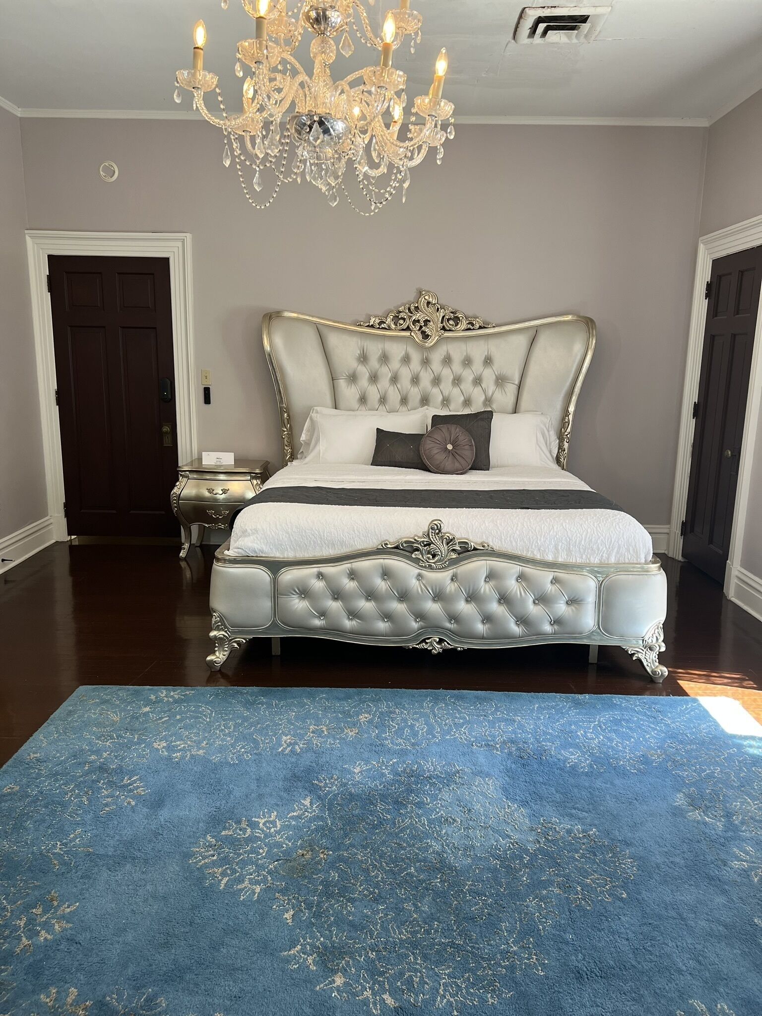 Un dormitorio con una cama grande, una araña y una alfombra azul.