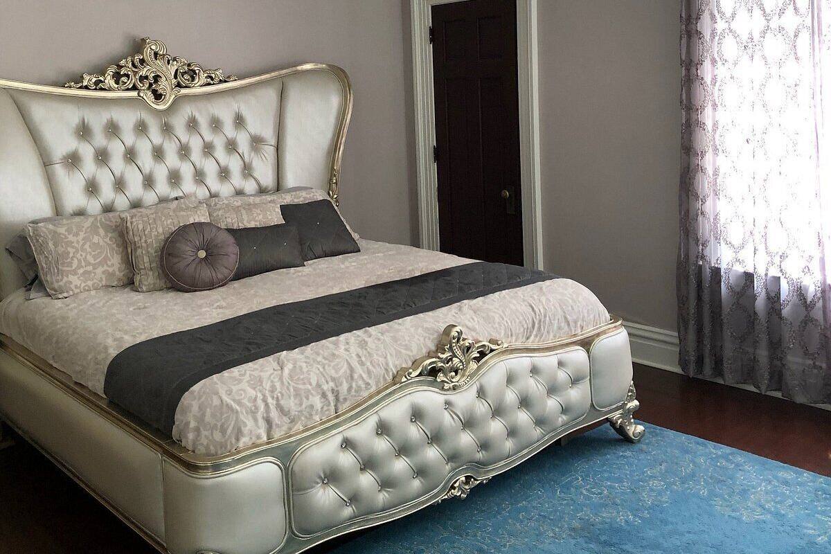 A bedroom with a tufted headboard, a large chandelier, and a patterned bedspread.