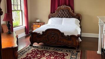 A bedroom with a large bed, a chandelier, a wooden dresser, and a red and black patterned rug.
