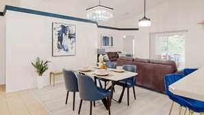 Un comedor moderno con una mesa dispuesta para cuatro, sillas azules y una lámpara de araña.