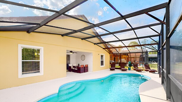Una piscina interior con un patio cubierto, una mesa de comedor y sillas de descanso.