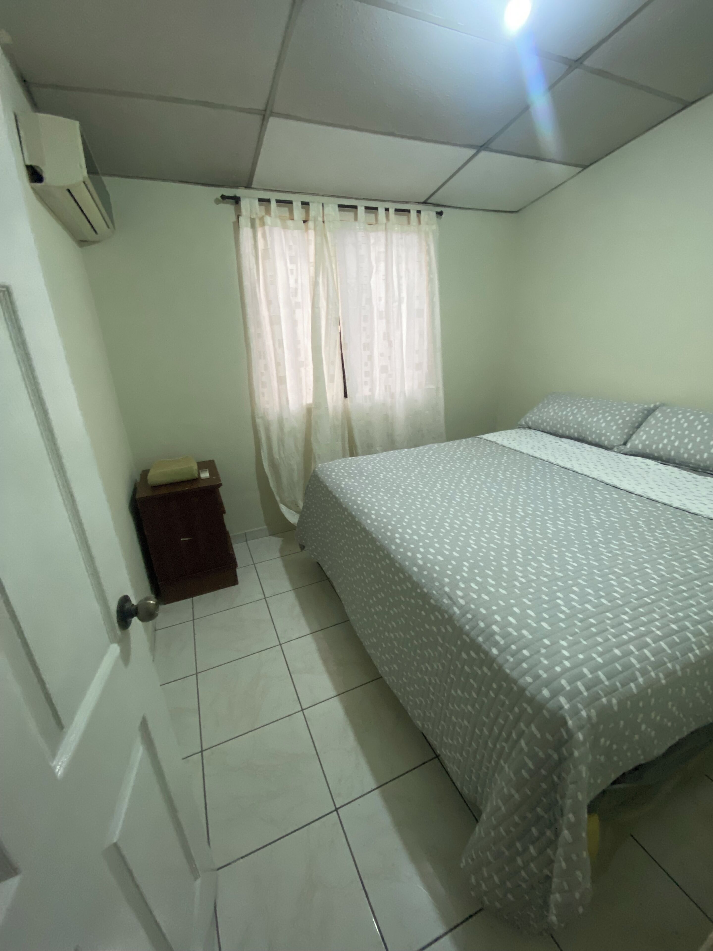 A bedroom with a bed, a nightstand, a window with curtains, and a ceiling light.