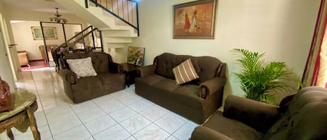 Una sala de estar con una escalera, un conjunto de sofás, una araña y un cuadro en la pared.