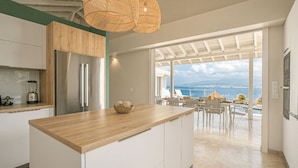 A modern kitchen with a wooden countertop, stainless steel appliances, and a view of the sea through large windows. - Tangarane offers two luxury villas with private pools and exceptional views over (LES TROIS ILETS)