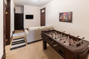 Una habitación con una mesa de fútbol de mesa, un sofá, un televisor en la pared y un cuadro.