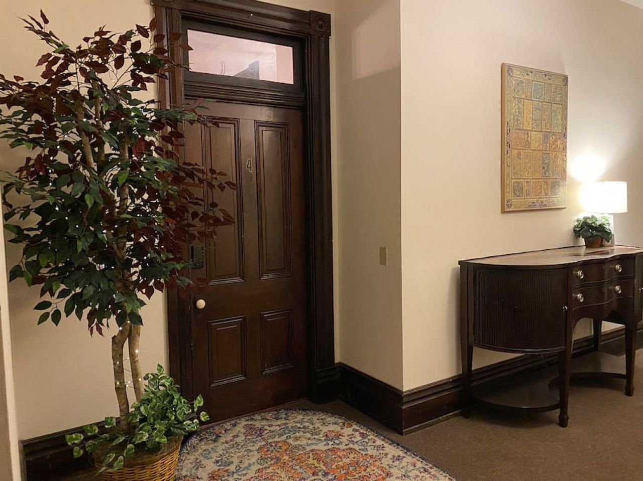 A wooden door with a small window, a dark wooden desk with drawers, a potted plant, and a patterned rug.
