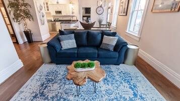 A living room with a dark blue sofa, patterned rug, and a wooden coffee table with a green plant.