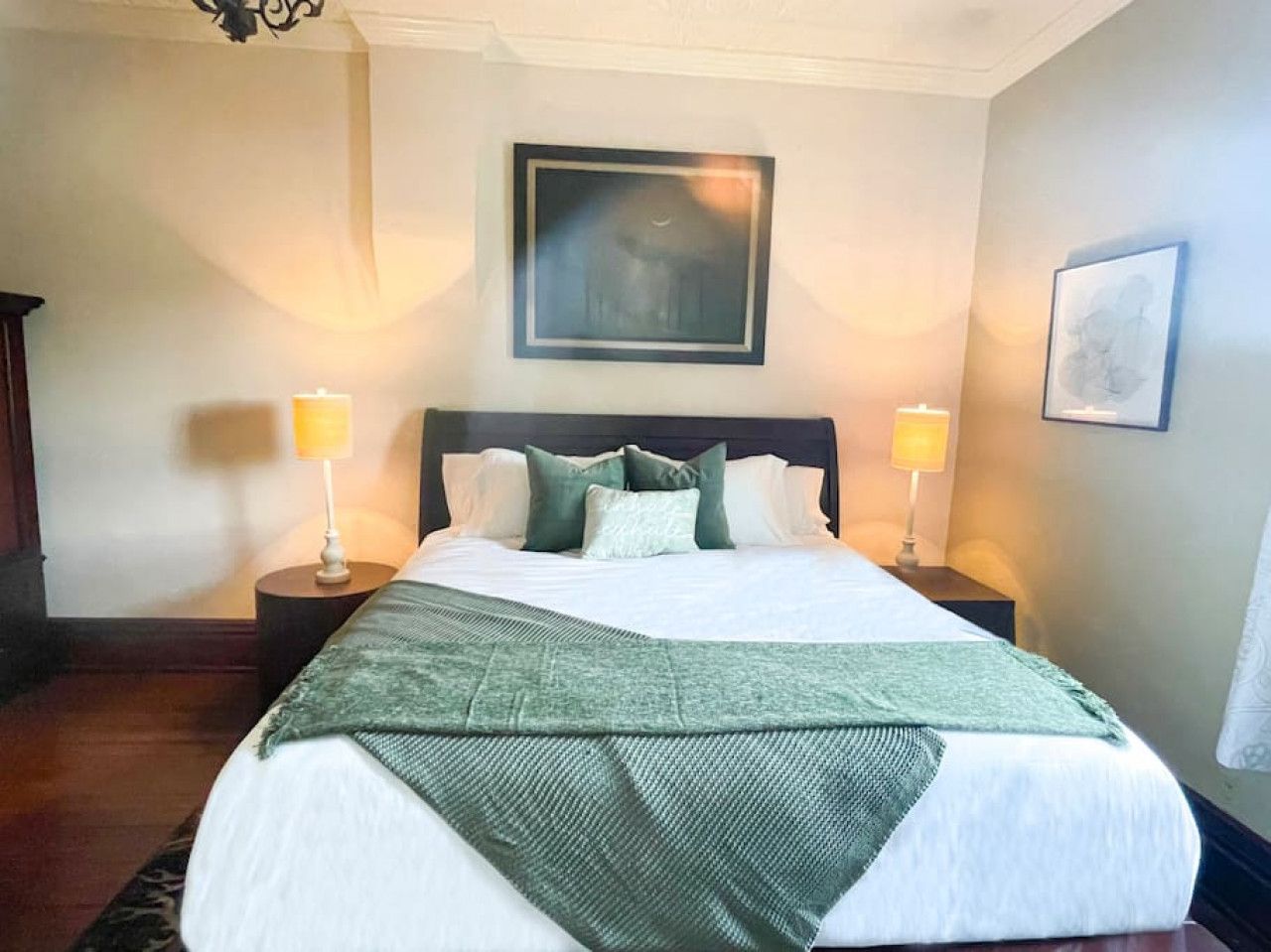 A hotel room with a large bed, two bedside lamps, a framed picture on the wall, and a patterned throw blanket.