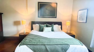 A hotel room with a large bed, two bedside lamps, a framed picture on the wall, and a patterned throw blanket.