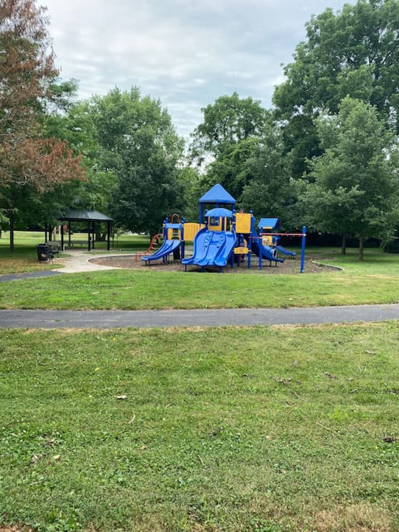 A playground with slides and climbing structures, surrounded by grass and trees.