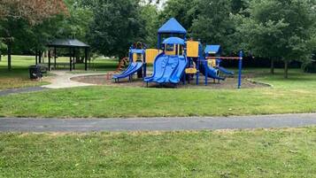 A playground with slides and climbing structures, surrounded by grass and trees.
