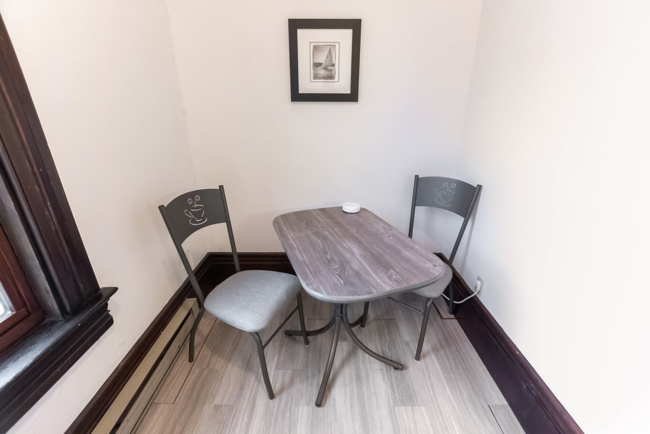 Un rincón comedor con una mesa y dos sillas, un cuadro enmarcado en la pared y una ventana con marco oscuro.