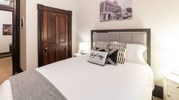 A hotel room with a large bed, a wooden door, a wall-mounted picture, and a bedside table with a lamp.