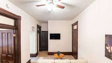 A living room with a ceiling fan, a flat-screen TV mounted on the wall, and a beige sofa.