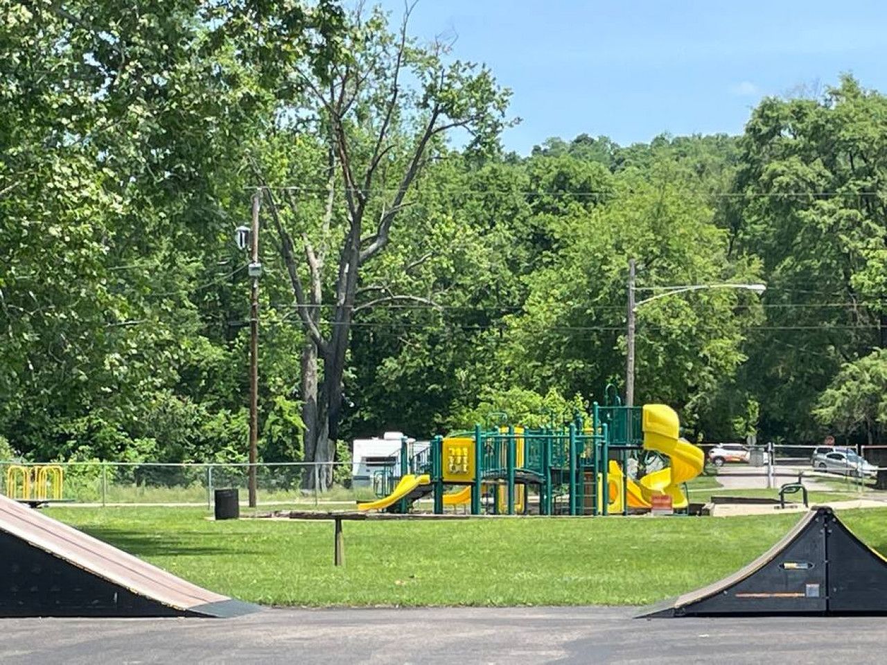 A playground with slides and climbing structures, surrounded by trees and a clear sky.