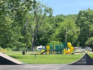 A playground with slides and climbing structures, surrounded by trees and a clear sky.