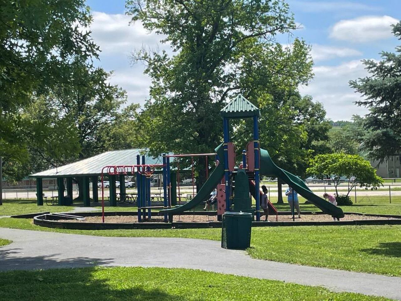 A playground with a slide and climbing structures, surrounded by grass and trees.