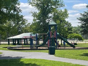Un parque infantil con un tobogán y estructuras para escalar, rodeado de césped y árboles.
