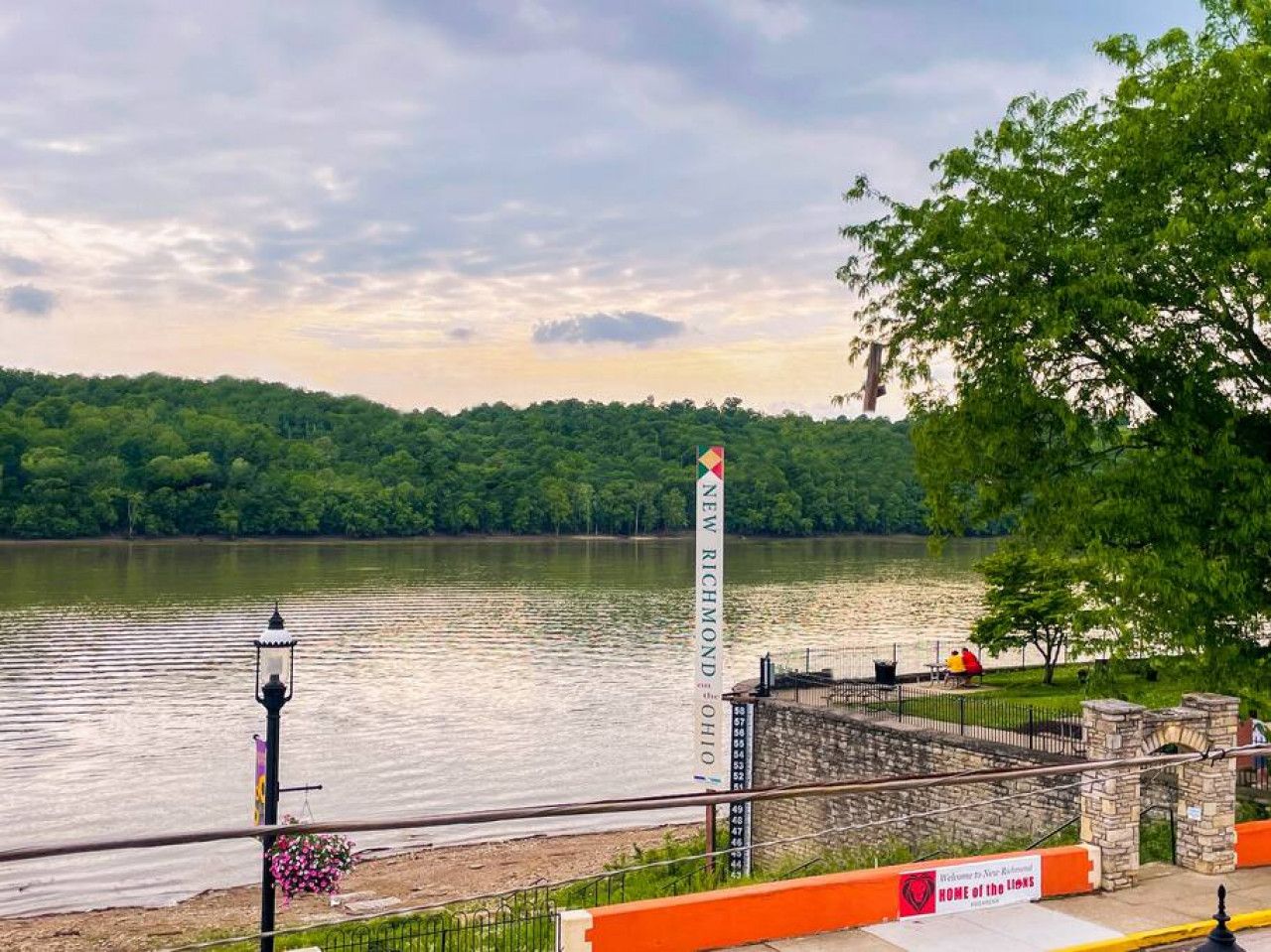 A waterfront view with a stone bridge, a lamppost, and a sign indicating a new development.