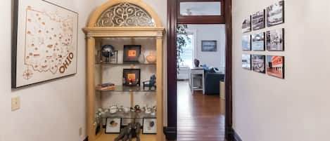 A hallway with a decorative cabinet, framed artwork, and a series of black-and-white photographs on the walls.