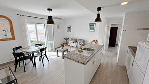 Una cocina moderna con una isla central, comedor con sillas y sala de estar con sofá.