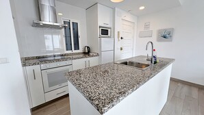 Una cocina moderna con armarios blancos, encimera de granito, electrodomésticos de acero inoxidable y un lavamanos integrado.
