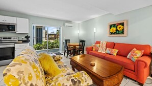 A modern living room with a red sofa, a wooden coffee table, and a kitchen area with white cabinets and a microwave.