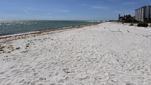 A beach with a clear sky, a sandy shore, and a building with multiple floors in the background.
