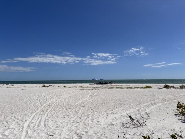 A beach with footprints leading to a group of people under umbrellas.