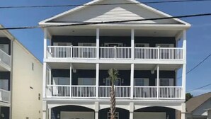 A two-story building with a central entrance, a small tree in front, and two garages on either side. - Blue SeaShell (North Myrtle Beach)