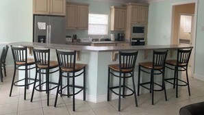A kitchen with a central island, bar stools, light-colored cabinets, and a refrigerator. - Blue SeaShell (North Myrtle Beach)