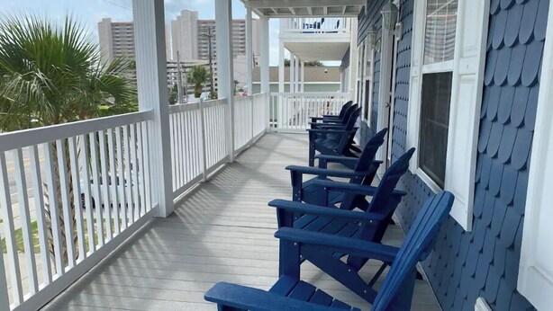 A covered porch with blue Adirondack chairs, white railings, and a view of the city skyline. - Blue SeaShell (North Myrtle Beach)