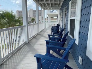 A covered porch with blue Adirondack chairs, white railings, and a view of the city skyline. - Blue SeaShell (North Myrtle Beach)