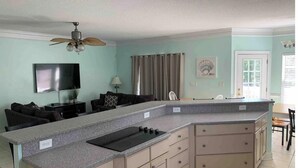 A modern kitchen with a large island, a ceiling fan, and a flat-screen TV. - Blue SeaShell (North Myrtle Beach)