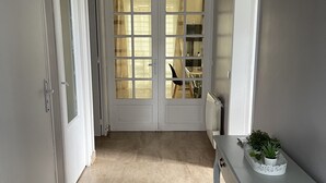 Un pasillo con una puerta blanca, una mesa blanca con una planta y una lámpara colgante negra.